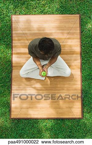 Man sitting indian style on mat outdoors, holding apple, high angle view View Large Photo Image Stock Image - Man sitting indian style on mat outdoors, holding apple, high angle view. Fotosearch