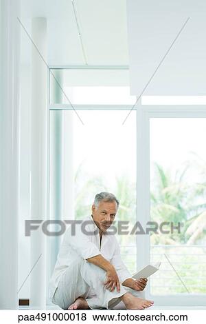 Mature man sitting on the ground, holding book, smiling at camera View Large Photo Image Stock Photo - Mature man sitting on the ground, holding book, smiling at camera. Fotosearch
