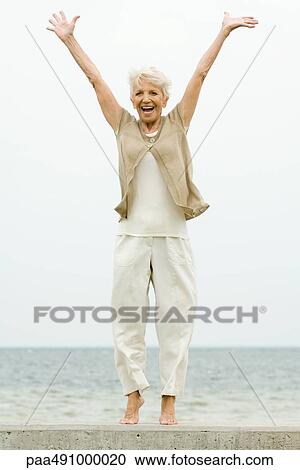 Senior woman standing on tiptoe at the beach, arms raised, smiling View Large Photo Image Stock Image - Senior woman standing on tiptoe at the beach, arms raised, smiling. Fotosearch