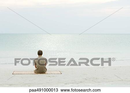 Teenage boy sitting at the beach, looking at the ocean, rear view View Large Photo Image Stock Image - Teenage boy sitting at the beach, looking at the ocean, rear view. Fotosearch