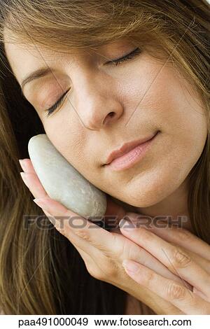 Woman holding smooth stone against cheek, eyes closed, close-up View Large Photo Image Stock Photo - Woman holding smooth stone against cheek, eyes closed, close-up. Fotosearch