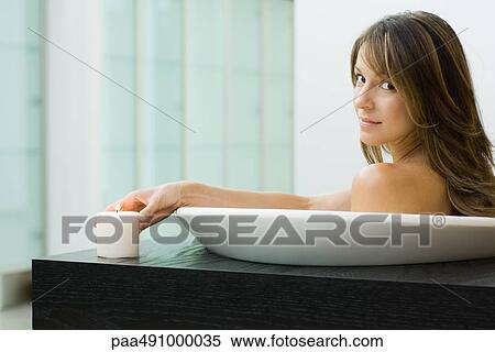 Woman sitting in bathtub, holding lit candle, smiling over shoulder at camera View Large Photo Image Stock Photography - Woman sitting in bathtub, holding lit candle, smiling over shoulder at camera. Fotosearch