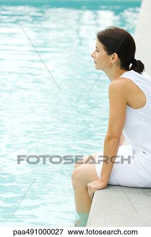 Woman sitting on edge of swimming pool, dipping feet in water, looking away View Large Photo Image Stock Photo - Woman sitting on edge of swimming pool, dipping feet in water, looking away. Fotosearch
