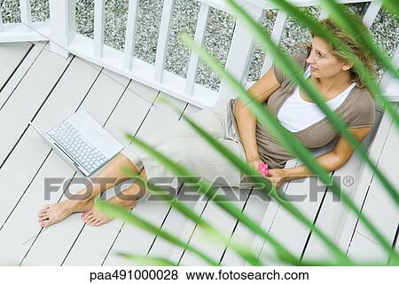 Woman sitting on porch next to laptop computer, holding flower, looking away, high angle view View Large Photo Image Stock Photo - Woman sitting on porch next to laptop computer, holding flower, looking away, high angle view. Fotosearch