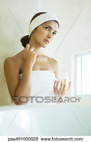 Young woman wrapped in towel applying perfume to neck, looking away View Large Photo Image Stock Photo - Young woman wrapped in towel applying perfume to neck, looking away. Fotosearch