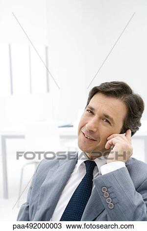 Stock Image - Businessman using cell phone, smiling at camera. Fotosearch