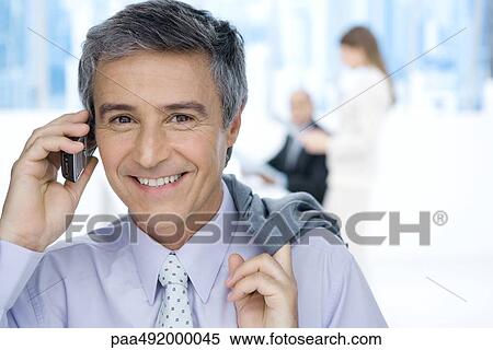 Mature businessman using cell phone in office, holding jacket over shoulder, smiling at camera View Large Photo Image Stock Photography - Mature businessman using cell phone in office, holding jacket over shoulder, smiling at camera. Fotosearch