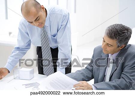 Two businessmen looking over documents together View Large Photo Image Stock Image - Two businessmen looking over documents together. Fotosearch
