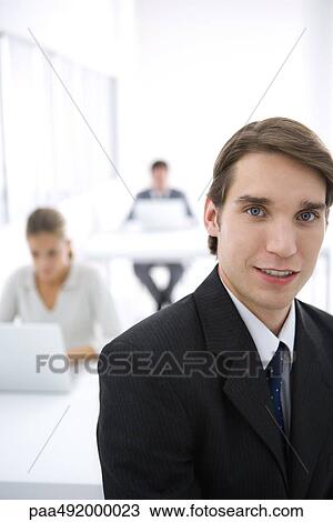 Stock Image - Young businessman in office, smiling at camera. Fotosearch