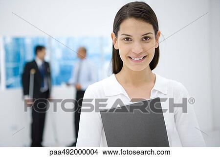 Picture - Young female office worker holding file, smiling at camera. Fotosearch