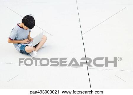Boy sitting cross-legged on the ground, using laptop, high angle view View Large Photo Image Stock Image - Boy sitting cross-legged on the ground, using laptop, high angle view. Fotosearch