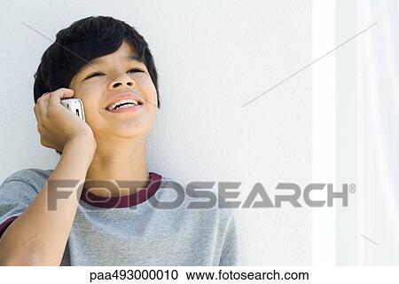 Stock Image - Boy using cell phone, looking up, smiling. Fotosearch