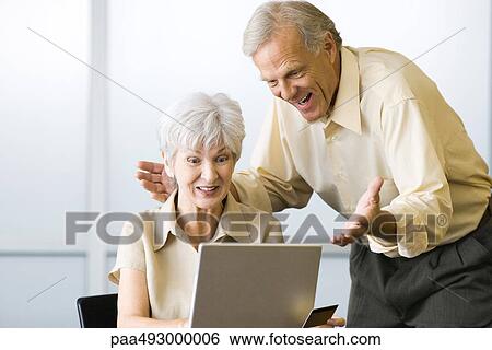 Excited mature couple looking at laptop computer together, woman holding credit card View Large Photo Image Stock Photograph - Excited mature couple looking at laptop computer together, woman holding credit card. Fotosearch