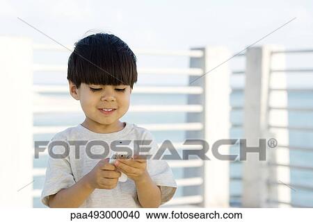 Little boy outdoors, looking down at cell phone, smiling View Large Photo Image Stock Image - Little boy outdoors, looking down at cell phone, smiling. Fotosearch