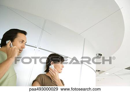 Man and woman indoors, looking away, both holding cell phone to ear, cropped View Large Photo Image Stock Photo - Man and woman indoors, looking away, both holding cell phone to ear, cropped. Fotosearch