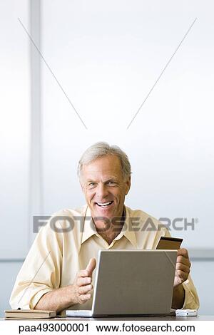 Stock Image - Man making on-line purchase with credit card, smiling at camera. Fotosearch