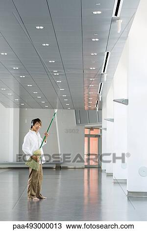 Man standing in lobby, playing air guitar with broom, listening to headphones, smiling at camera View Large Photo Image Stock Image - Man standing in lobby, playing air guitar with broom, listening to headphones, smiling at camera. Fotosearch