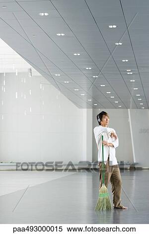 Man standing in lobby, resting arm on broom, listening to headphones View Large Photo Image Stock Photography - Man standing in lobby, resting arm on broom, listening to headphones. Fotosearch