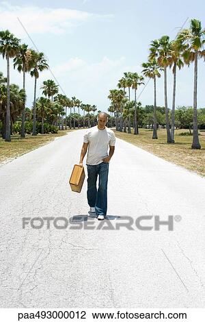 Man walking down center of road, carrying suitcase, listening to headphones View Large Photo Image Stock Image - Man walking down center of road, carrying suitcase, listening to headphones. Fotosearch