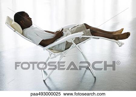 Teenage boy reclining in chair, looking down at cell phone View Large Photo Image Stock Photography - Teenage boy reclining in chair, looking down at cell phone. Fotosearch