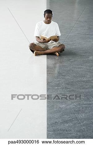 Teenage boy sitting cross-legged on the floor, reading a book, listening to headphones View Large Photo Image Stock Photograph - Teenage boy sitting cross-legged on the floor, reading a book, listening to headphones. Fotosearch