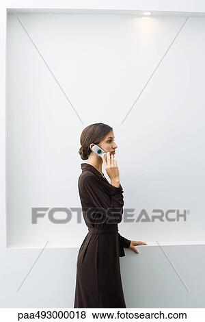Well-dressed young female using cell phone, standing, side view View Large Photo Image Stock Photo - Well-dressed young female using cell phone, standing, side view. Fotosearch