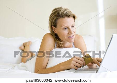 Woman lying on stomach in bed, using laptop and credit card View Large Photo Image Stock Image - Woman lying on stomach in bed, using laptop and credit card. Fotosearch