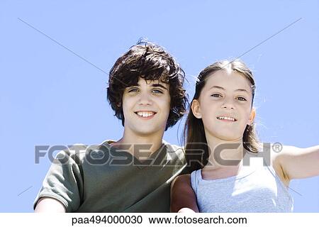Stock Image - Brother and sister smiling at camera, low angle view, portrait. Fotosearch