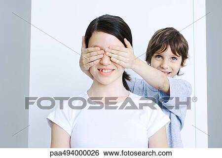 Stock Photograph - Brother covering his sisters eyes with his hands, smiling. Fotosearch