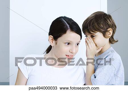 Stock Image - Brother whispering to his sister, hand covering mouth. Fotosearch