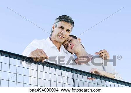 Picture - Couple looking down over wire fence at camera, low angle view. Fotosearch