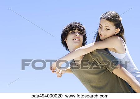 Teen boy carrying younger sister on his back, both smiling at each other, low angle view View Large Photo Image Stock Image - Teen boy carrying younger sister on his back, both smiling at each other, low angle view. Fotosearch