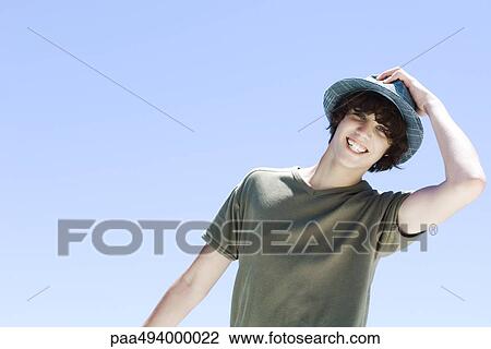Teenage boy smiling at camera, putting on a hat View Large Photo Image Stock Image - Teenage boy smiling at camera, putting on a hat. Fotosearch