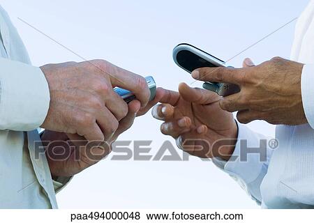 Two men face to face, holding cell phones, cropped view of hands View Large Photo Image Stock Photo - Two men face to face, holding cell phones, cropped view of hands. Fotosearch