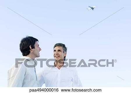 Stock Photograph - Two men talking to each other, airplane high in the background. Fotosearch