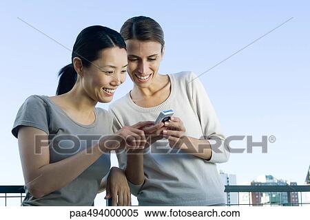 Stock Photography - Two women looking at camera phone, smiling. Fotosearch