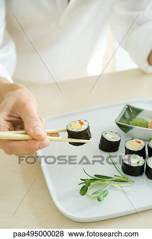 Person using chopsticks to pick up a sushi roll, cropped view View Large Photo Image Stock Photo - Person using chopsticks to pick up a sushi roll, cropped view. Fotosearch