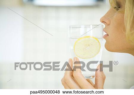 Woman holding a glass of water with a slice of lemon up to her lips, profile View Large Photo Image Stock Photo - Woman holding a glass of water with a slice of lemon up to her lips, profile. Fotosearch