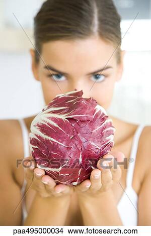 Woman holding a head of radicchio lettuce, partially obscuring her face, looking at camera View Large Photo Image Picture - Woman holding a head of radicchio lettuce, partially obscuring her face, looking at camera. Fotosearch