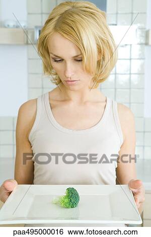 Woman holding plate with a single piece of broccoli, looking down View Large Photo Image Stock Photograph - Woman holding plate with a single piece of broccoli, looking down. Fotosearch