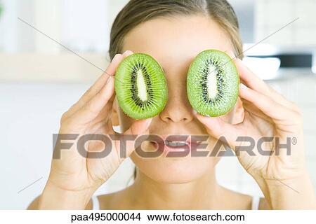 Woman holding two kiwi halves up to her eyes like binoculars, headshot View Large Photo Image Picture - Woman holding two kiwi halves up to her eyes like binoculars, headshot. Fotosearch