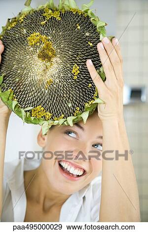 Stock Photo - Woman holding up large dried flower head, looking up, smiling. Fotosearch
