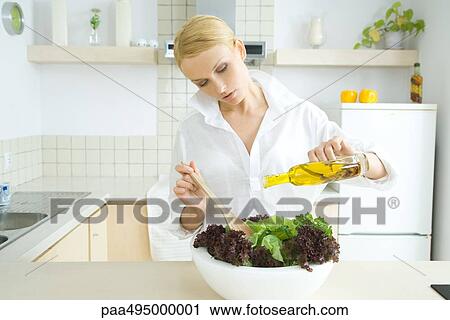 Woman standing in kitchen, pouring olive oil over salad View Large Photo Image Stock Image - Woman standing in kitchen, pouring olive oil over salad. Fotosearch