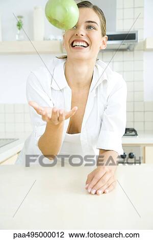 Woman with toothy smile tossing an apple in the air, in kitchen View Large Photo Image Stock Image - Woman with toothy smile tossing an apple in the air, in kitchen. Fotosearch