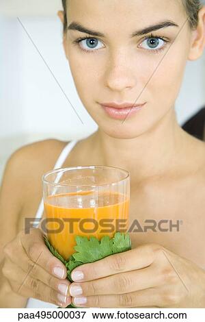 Stock Photo - Young woman holding a glass of vegetable juice, looking at camera, head and shoulders. Fotosearch