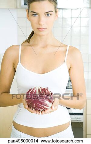 Picture - Young woman holding a head of radicchio lettuce in kitchen. Fotosearch
