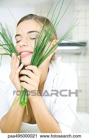Stock Image - Young woman holding chives up to face, eyes closed. Fotosearch