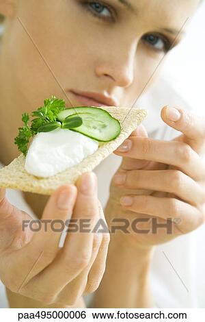 Young woman holding up cracker topped with cucumbers and cheese spread, cropped View Large Photo Image Stock Photograph - Young woman holding up cracker topped with cucumbers and cheese spread, cropped. Fotosearch
