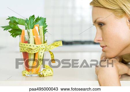 Young woman looking at glass full of vegetables with a measuring tape bow, profile View Large Photo Image Stock Image - Young woman looking at glass full of vegetables with a measuring tape bow, profile. Fotosearch