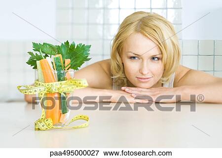 Young woman looking at glass of fresh vegetables with a measuring tape bow View Large Photo Image Stock Photo - Young woman looking at glass of fresh vegetables with a measuring tape bow. Fotosearch
